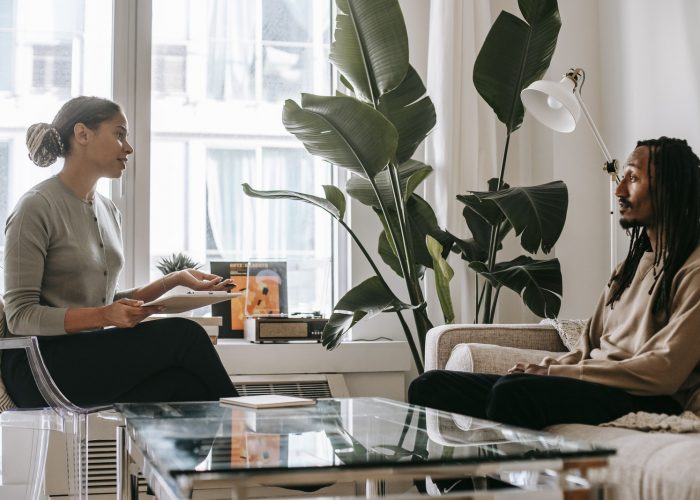 Side view of professional female African American therapist sitting in front of black male patient during psychotherapy session in office